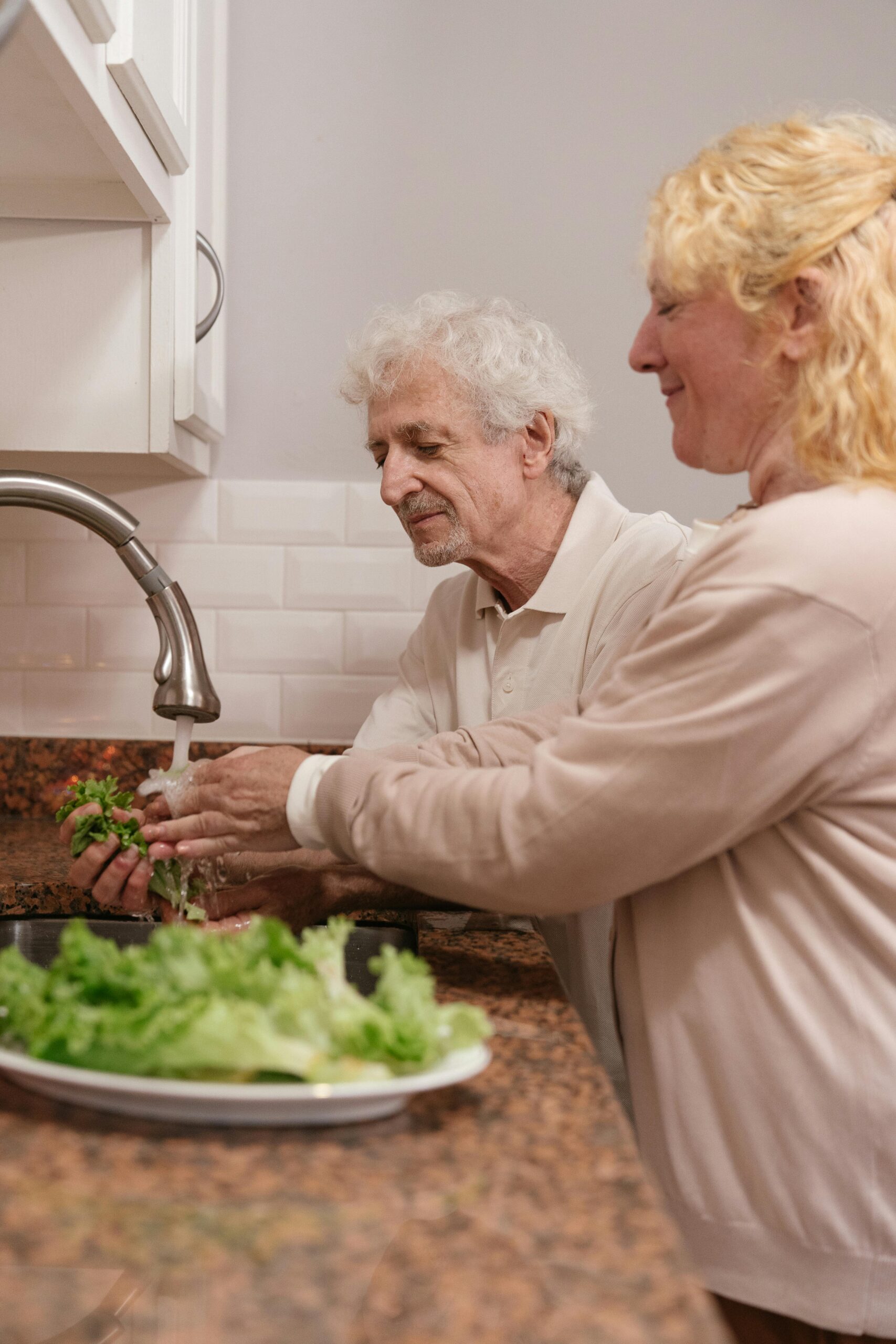 Elderly couple washing lettuce in a home kitchen, promoting healthy lifestyle and togetherness.