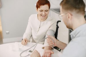 Man assisting elderly woman with blood pressure check at home in a friendly atmosphere.